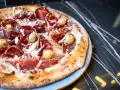 Pizza con jamón serrano, aceitunas y queso rallado, perfecta para saber donde comer en Menorca.