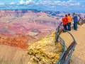 Tres personas admiran la inmensidad del cañón del Colorado, con sus capas rocosas de tonos rojizos y un río turquesa serpenteando en el fondo.