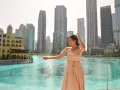 Mujer disfrutando de su viaje a Dubai, con rascacielos y una fuente de agua de fondo.