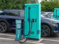 Coches eléctricos cargando. Las ventajas y desventajas de los coches eléctricos se reflejan en esta escena de carga, con un cartel que invita a descargar una app para ahorrar.