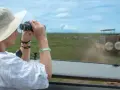 Mujer con sombrero y binoculares observa cebras en la sabana, disfrutando de su viaje a Tanzania.