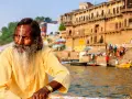 Un hombre con barba y marca en la frente navega en el Ganges, una escena típica al viajar a la India.