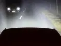 Luces de carretera o largas iluminan la noche, revelando un coche adelante y el camino.