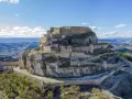 Castillo de Morella sobre un peñón rocoso, con murallas y edificios de piedra bajo un cielo azul con nubes.
