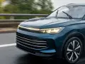 Un elegante coche seminuevo de color azul oscuro circula por una carretera mojada, con las luces encendidas.