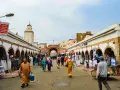 Mercado vibrante en Essaouira que ver: gente comprando ropa y artesanías bajo arcos blancos, con una mezquita al fondo.