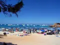 Playa con gente, sombrillas y barcos en el mar azul. Un día perfecto para ver qué ver en Formentera.
