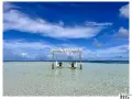 Dos personas disfrutan de columpios en forma de luna sobre aguas cristalinas. Un cartel dice "Visit Dhangethi", mostrando que las Maldivas low cost son posibles.