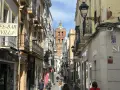 Calle comercial con edificios antiguos y un campanario al fondo. Descubre qué ver en Zafra y disfruta de su encanto.