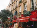 Calle parisina con restaurantes y mesas al aire libre, ideal para comer barato en París. Un tren decorativo adorna un toldo rojo.