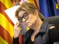 Mujer con gafas y chaleco oscuro, con banderas de España y Europa al fondo. Planeando su próximo viaje por España.