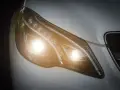 Primer plano de un faro de coche moderno con luces cortas encendidas, un símbolo de visibilidad y seguridad en la carretera.
