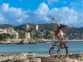 Escultura de aves metálicas en primer plano, con el castillo de Moraira y el puerto al fondo. Descubre qué ver en Moraira.