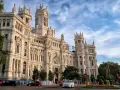 Un día en Madrid: el Palacio de Cibeles, un taxi blanco y coches circulan bajo un cielo azul con nubes.