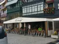Gente disfrutando de una comida en Lekeitio, sentados en mesas al aire libre bajo un toldo blanco.