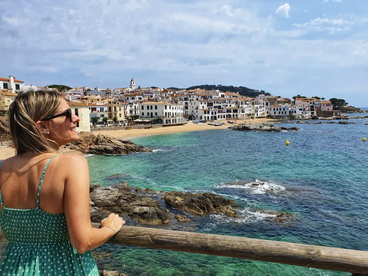 Mujer sonríe mirando el mar turquesa y las casas blancas de Calella de Palafrugell.