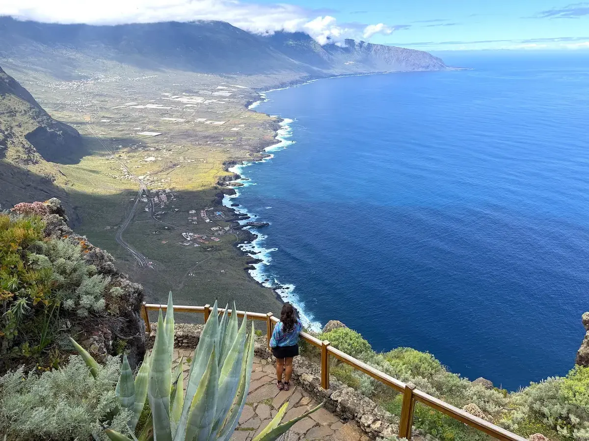Mujer admira la costa de El Hierro, con el mar azul intenso y montañas verdes.