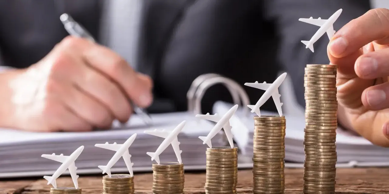 Pequeños aviones sobre pilas de monedas crecientes, simbolizando cómo viajar barato es posible con planificación.