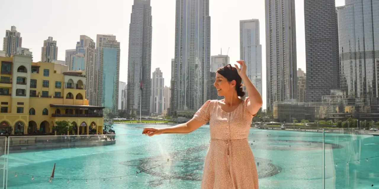 Mujer disfrutando de su viaje a Dubai, con rascacielos y una fuente de agua de fondo.