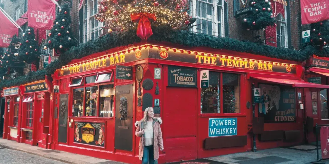 Una mujer pasea por la calle empedrada frente al icónico pub The Temple Bar en Dublín, decorado para Navidad. ¡Una excelente idea de qué hacer en Dublín!