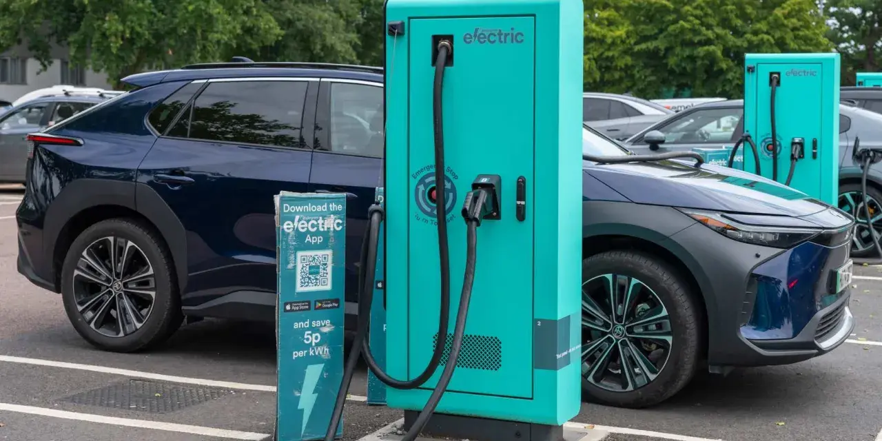 Coches eléctricos cargando. Las ventajas y desventajas de los coches eléctricos se reflejan en esta escena de carga, con un cartel que invita a descargar una app para ahorrar.