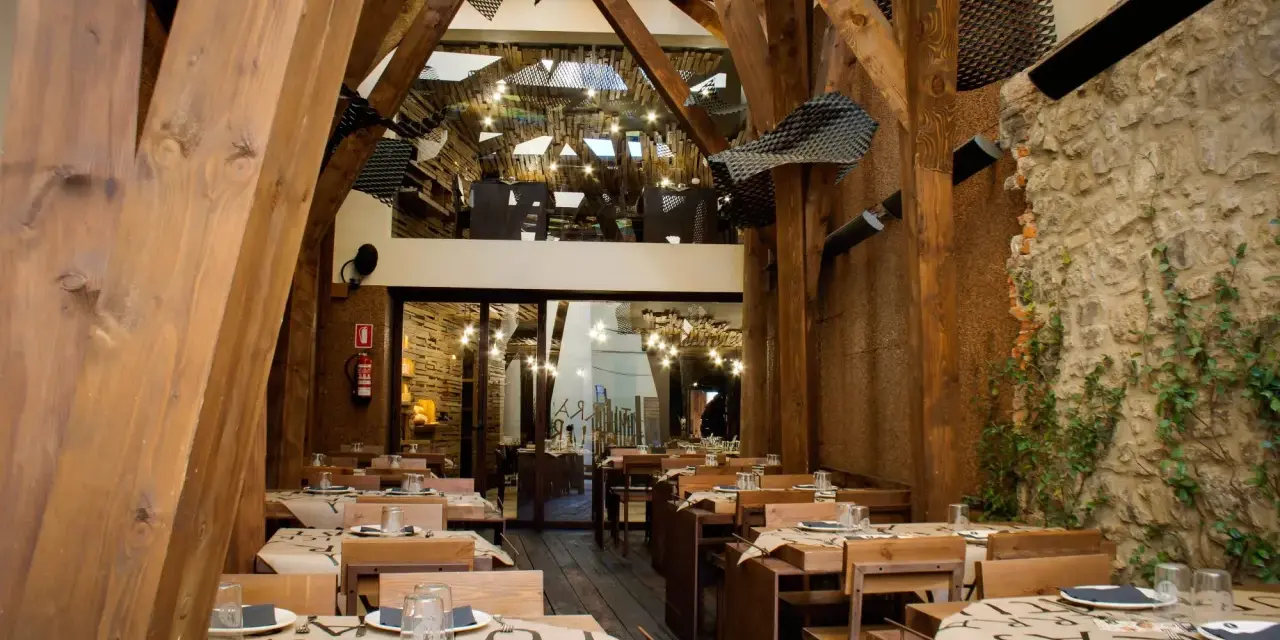 Mesas puestas en un restaurante rústico con vigas de madera y paredes de piedra, ideal para comer en Avilés.
