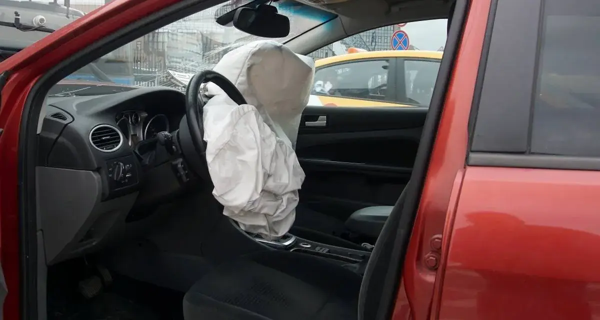 Interior de coche rojo con airbag del conductor desplegado, indicando la dirección del vehículo activa o pasiva tras un impacto.