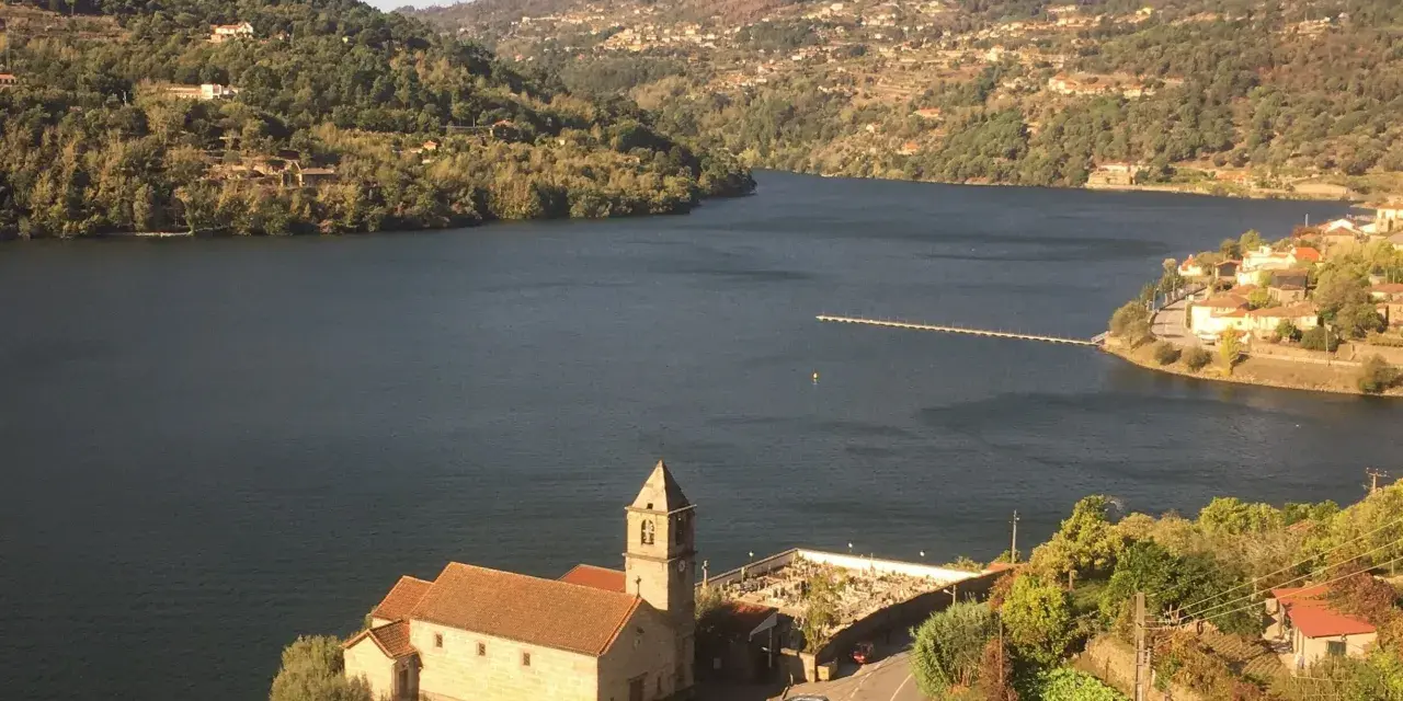 Un pueblo pintoresco a orillas de un río, con una iglesia y un cementerio. Las colinas verdes y las casas se extienden hasta donde alcanza la vista. ¡Un lugar ideal para ir a toro!