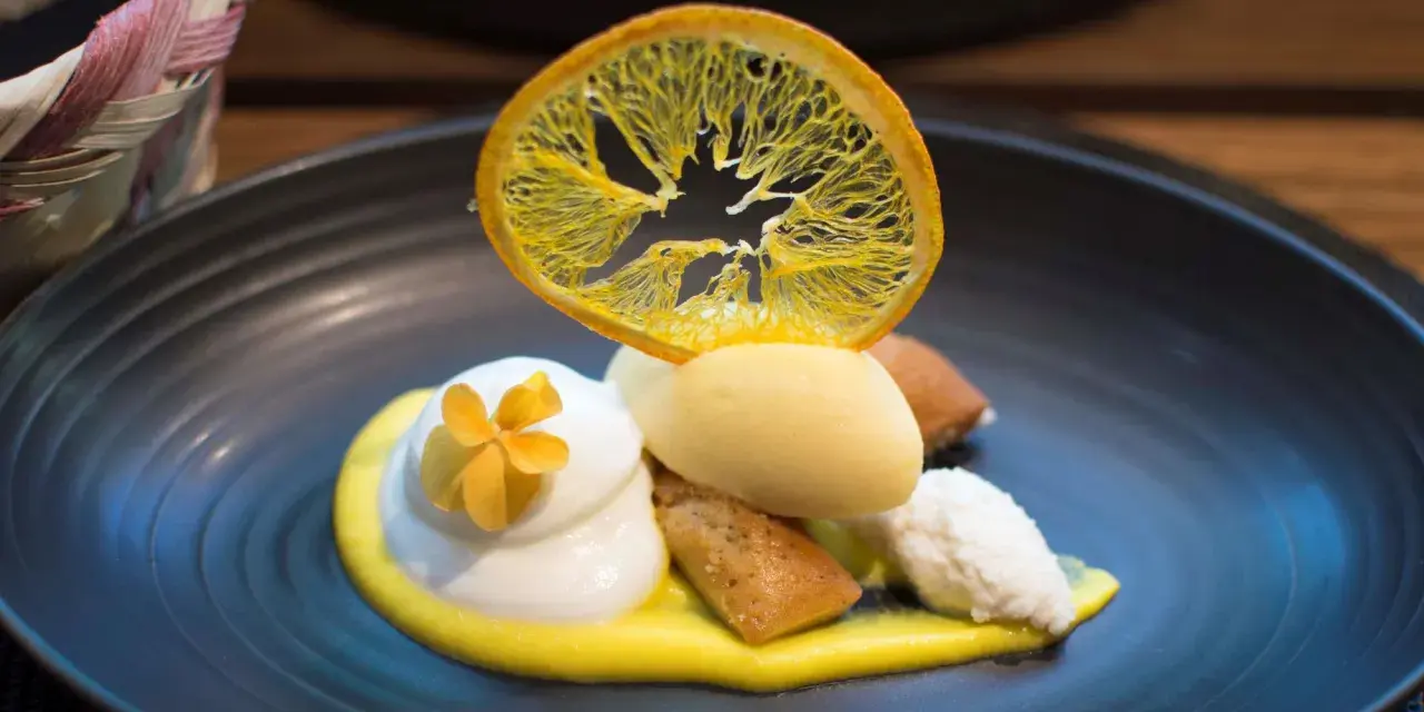 Postre de autor con helado de limón, merengue, bizcocho y naranja deshidratada. ¡Una delicia para saber dónde comer en Barcelona!