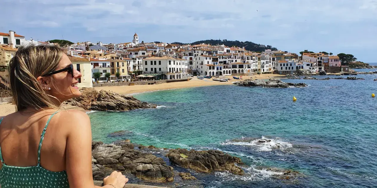 Mujer sonríe mirando el mar turquesa y las casas blancas de Calella de Palafrugell.