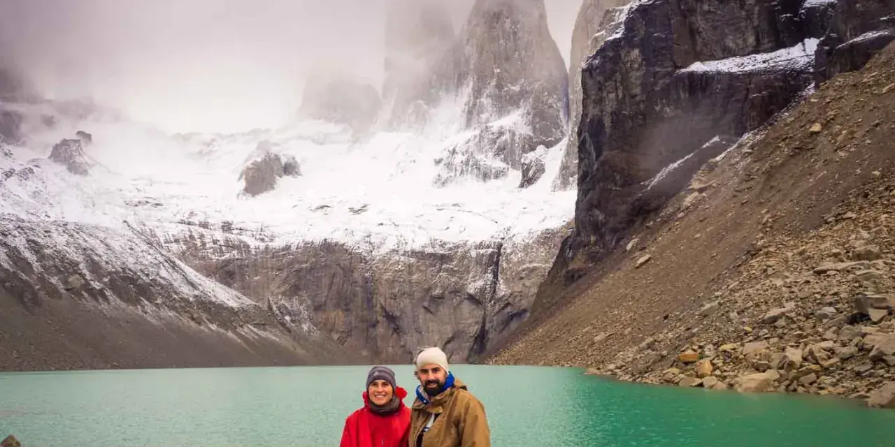 Pareja posa frente a un lago turquesa y montañas nevadas, un paisaje imperdible que ver en Chile.