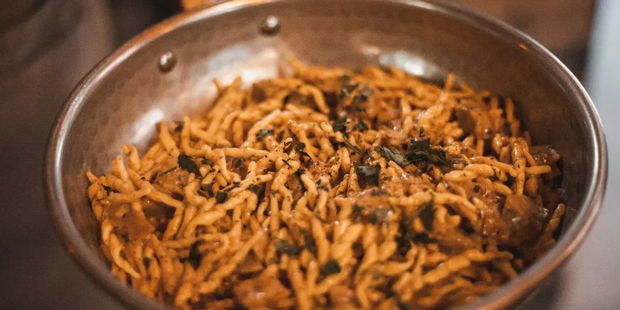 Pasta con salsa cremosa y hierbas en sartén. ¡Una deliciosa opción para saber dónde comer en Madrid!