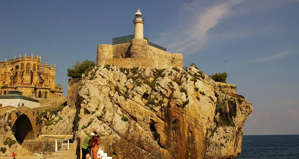Descubre qué ver en Castro Urdiales: un faro en un castillo sobre rocas, con una iglesia gótica al fondo y gente paseando.