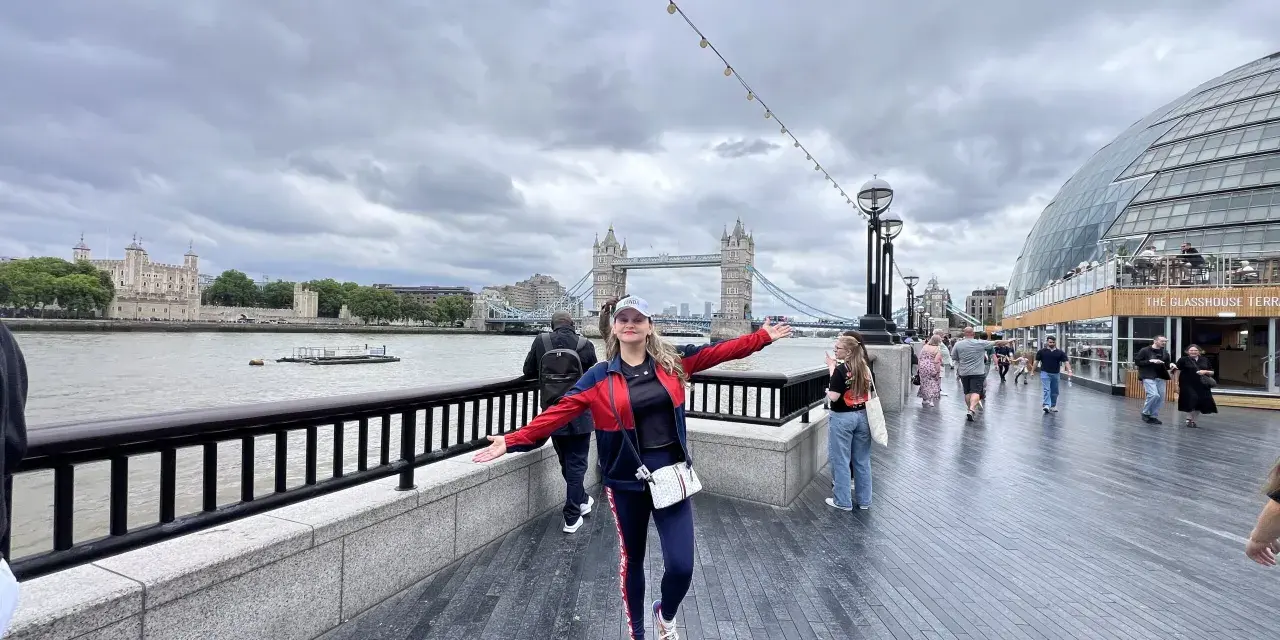 Mujer sonriente con brazos extendidos en Londres, con la Torre de Londres y el Tower Bridge al fondo. ¡Excelentes consejos para viajar a Londres!