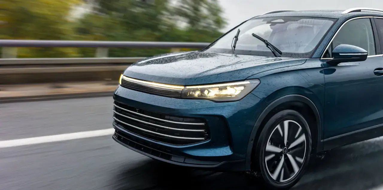 Un elegante coche seminuevo de color azul oscuro circula por una carretera mojada, con las luces encendidas.
