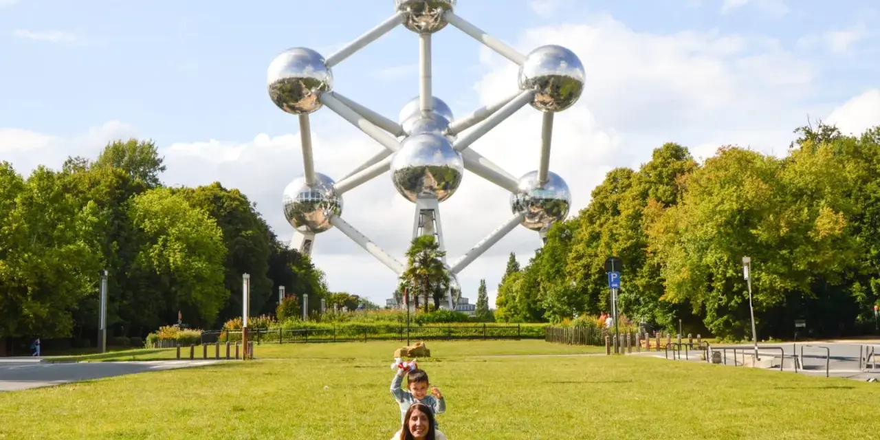 Familia posa frente al Atomium, un icono de que ver en Bruselas. Un niño salta detrás de su madre en el césped.
