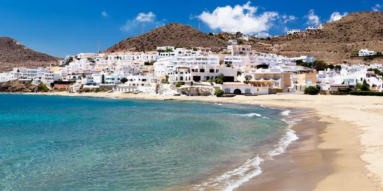 Pueblo blanco a orillas del mar turquesa, ideal para descubrir qué ver en Cabo de Gata. Playas doradas y casas encaladas bajo un cielo azul.