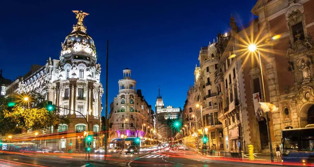 Noche vibrante en Madrid, con edificios iluminados y estelas de luz de coches. ¡Un fin de semana en Madrid inolvidable!