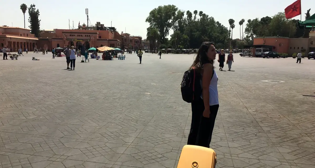 Una mujer con mochila y maleta amarilla en una plaza de Marruecos. Piensa en qué llevar a Marruecos para este viaje.