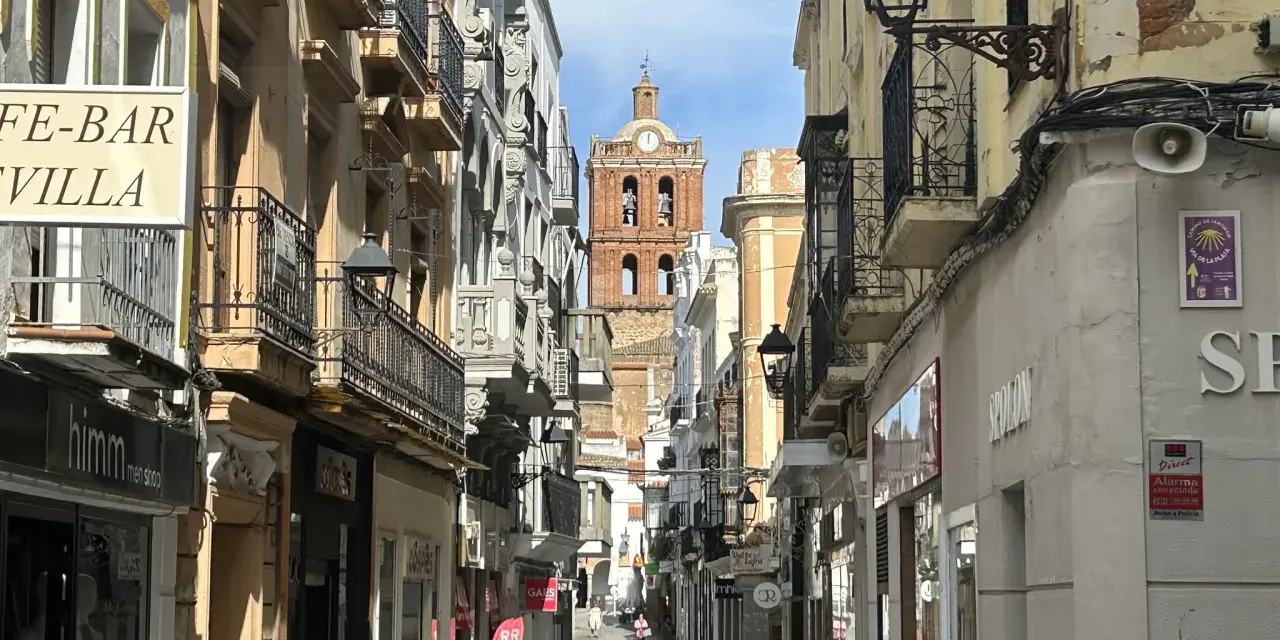 Calle comercial con edificios antiguos y un campanario al fondo. Descubre qué ver en Zafra y disfruta de su encanto.