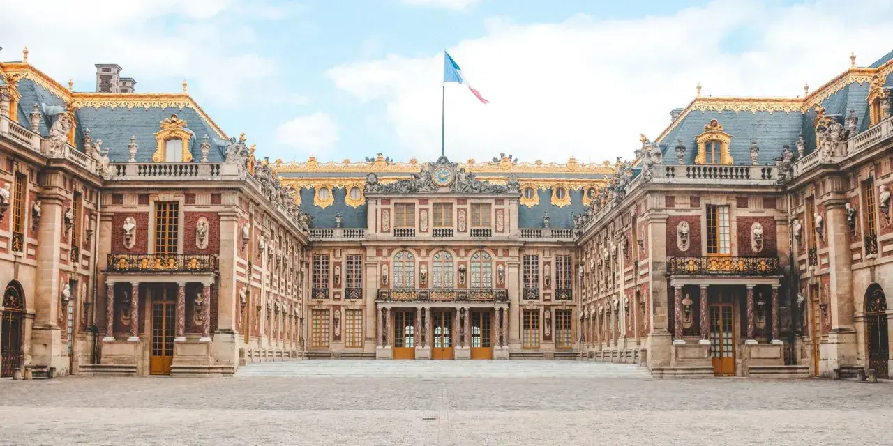 Palacio de Versalles, una visita obligada si buscas qué ver en París en 2 días. Majestuosa arquitectura y bandera francesa ondeando.