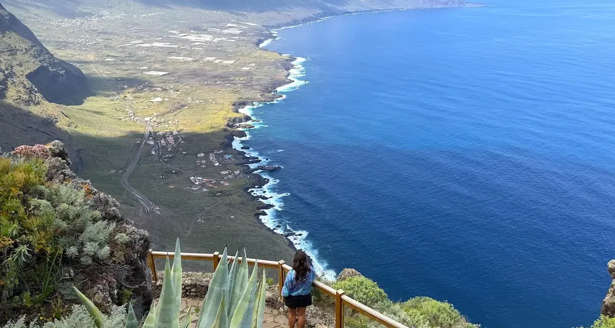 Mujer admira la costa de El Hierro, con el mar azul intenso y montañas verdes.