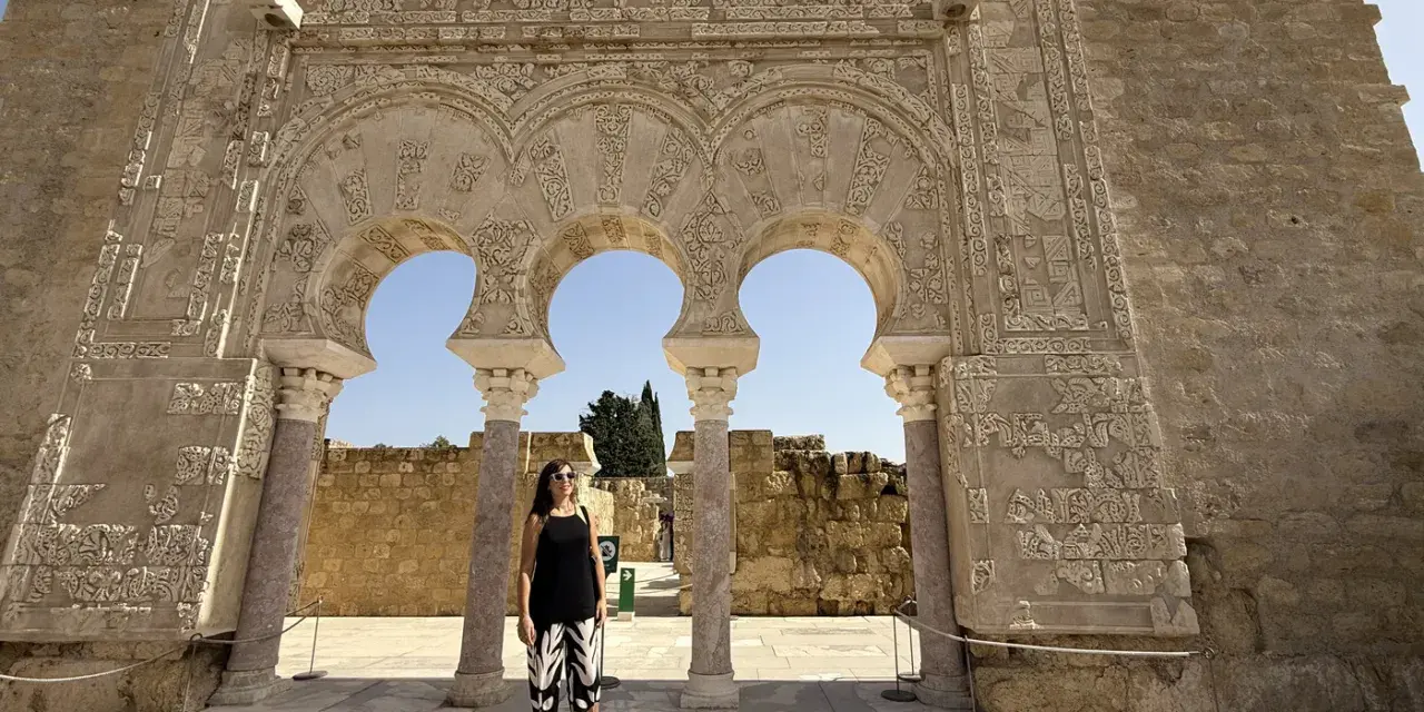 Mujer posa ante arcos de Medina Azahara. Se puede visitar Medina Azahara por libre, explorando su rica historia y arquitectura.