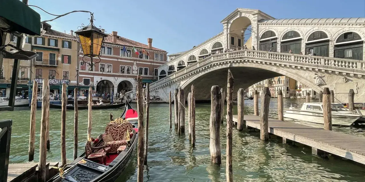Góndola esperando en el canal, con el Puente de Rialto al fondo. Ideas para que ver en Venecia en dos días.