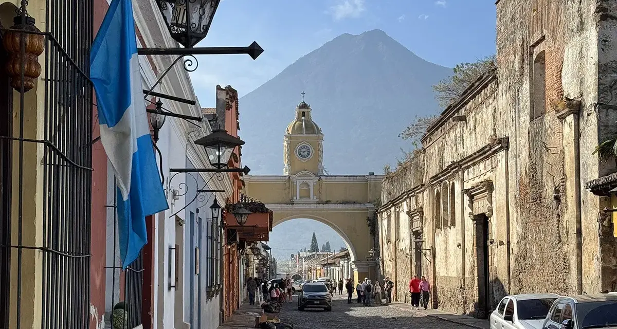 Calle empedrada en Antigua Guatemala, con el arco de Santa Catalina y el volcán de Agua al fondo. Ideal para descubrir qué ver en Antigua Guatemala.