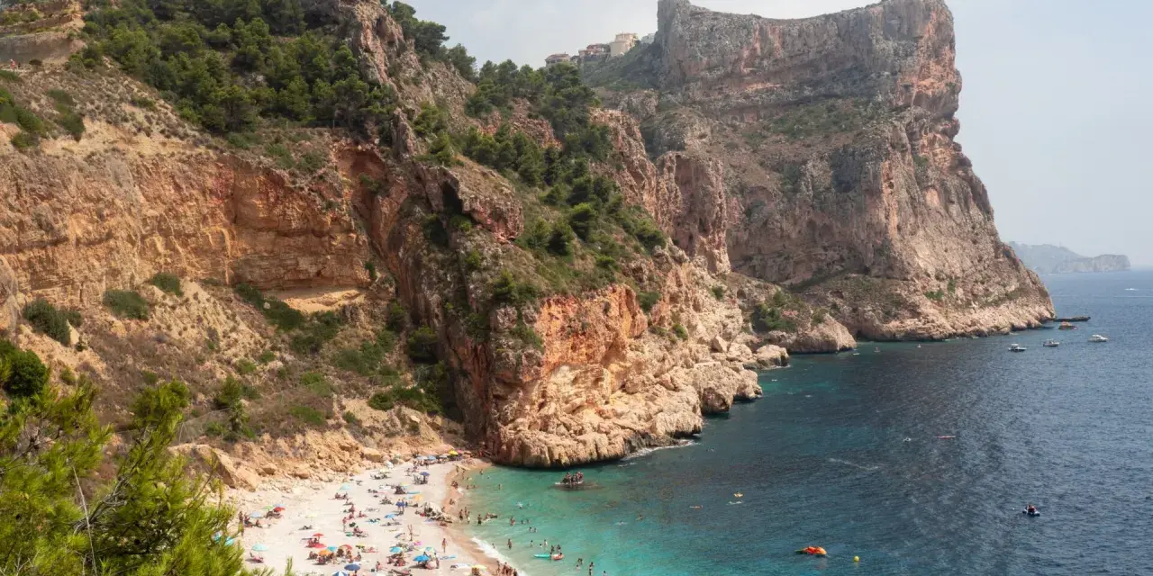Playa con acantilados y gente disfrutando del sol y el mar. Un plan perfecto para saber qué ver en Alicante provincia en una semana.