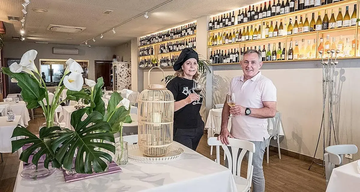 Pareja sonriente en un restaurante con estanterías llenas de vino. Un lugar ideal para saber donde comer en Logroño.