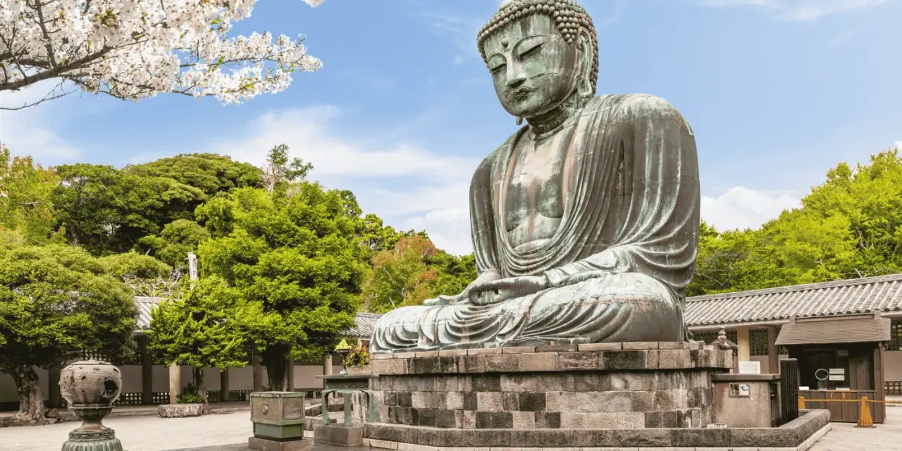 El Gran Buda de bronce, una maravilla que ver en Kamakura, sentado serenamente bajo cerezos en flor y rodeado de exuberante vegetación.
