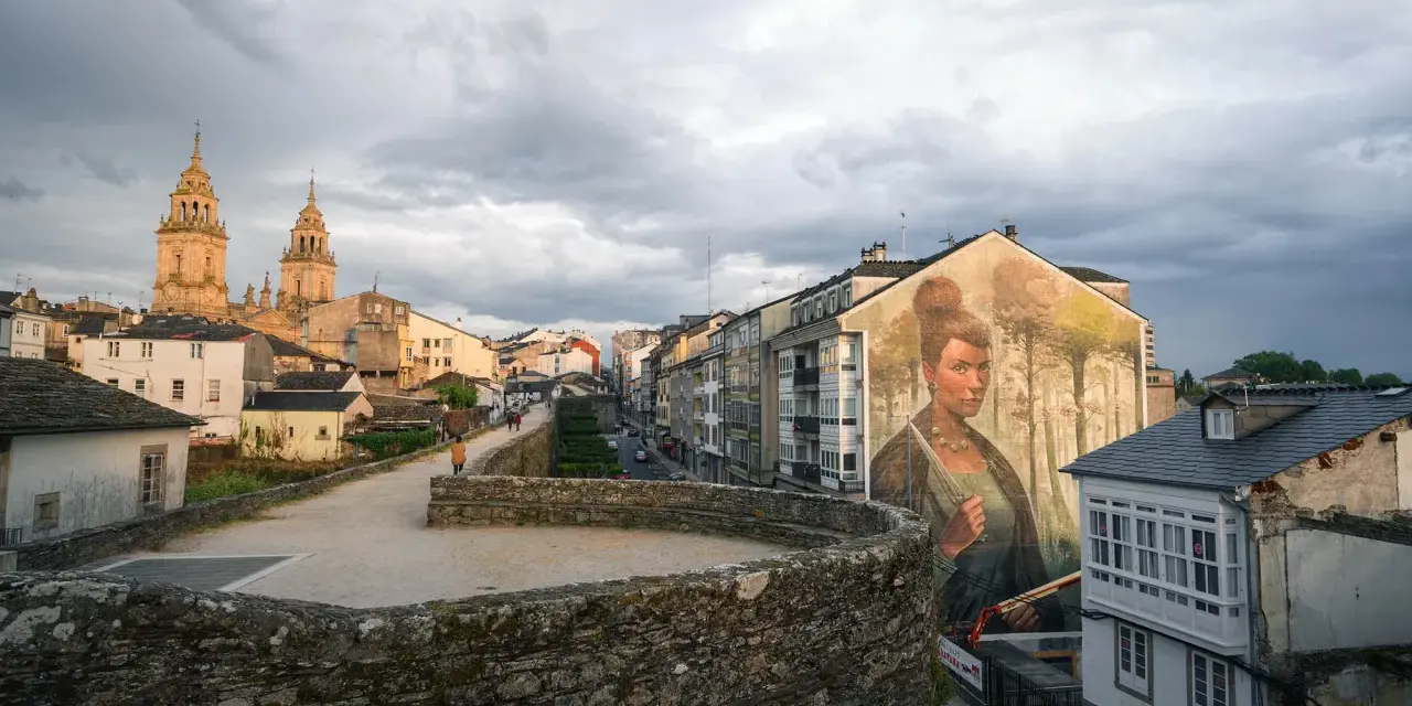 Mural de mujer en edificio, con la muralla romana y la catedral al fondo. Imprescindible que ver en Lugo.