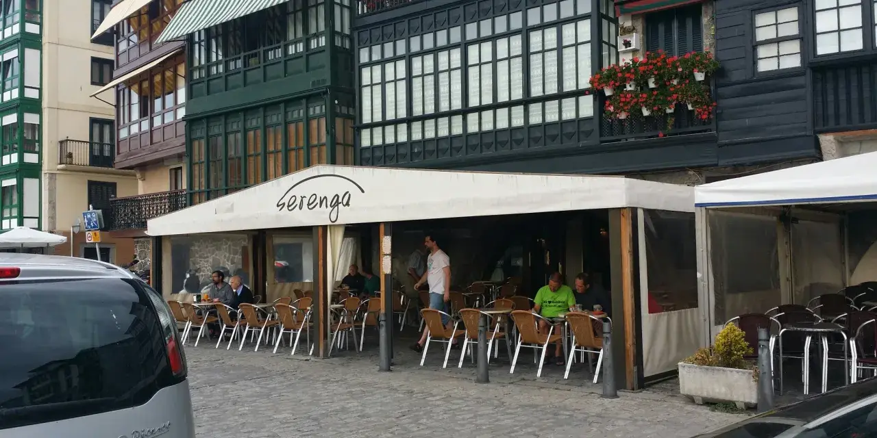 Gente disfrutando de una comida en Lekeitio, sentados en mesas al aire libre bajo un toldo blanco.